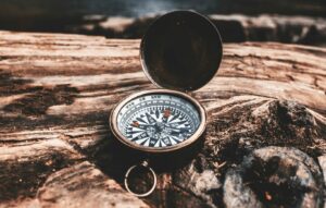 brass-colored-compass-on-brown-wooden-tree-stump-in-front-of-waterfalls-during-daytime